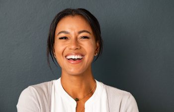 Smiling woman with dark hair against a dark gray background, wearing a white blouse and light cardigan.